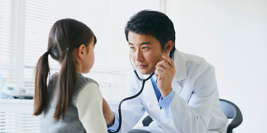 A doctor examining a young patient with a stethoscope in a bright clinic room